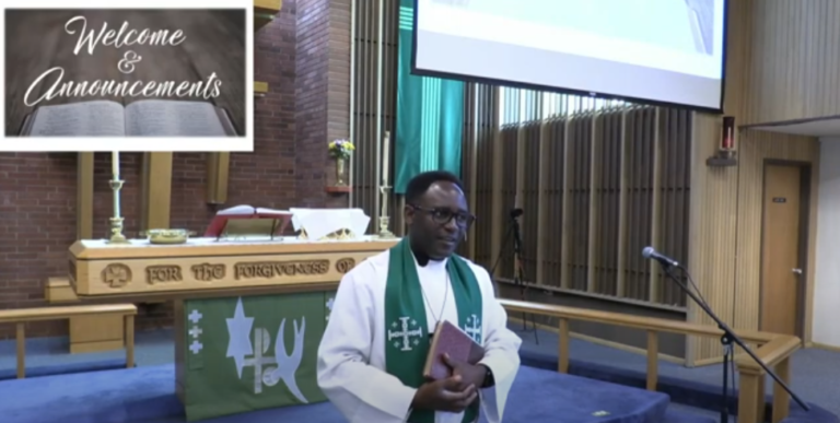 A pastor in religious attire, holding a book, stands in front of an altar in a church. The altar is adorned with a cross and communion items. A projection screen displays "Welcome & Announcements.